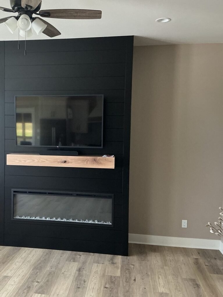 TV mounted on a black shiplap accent wall above a wood mantel and electric fireplace
